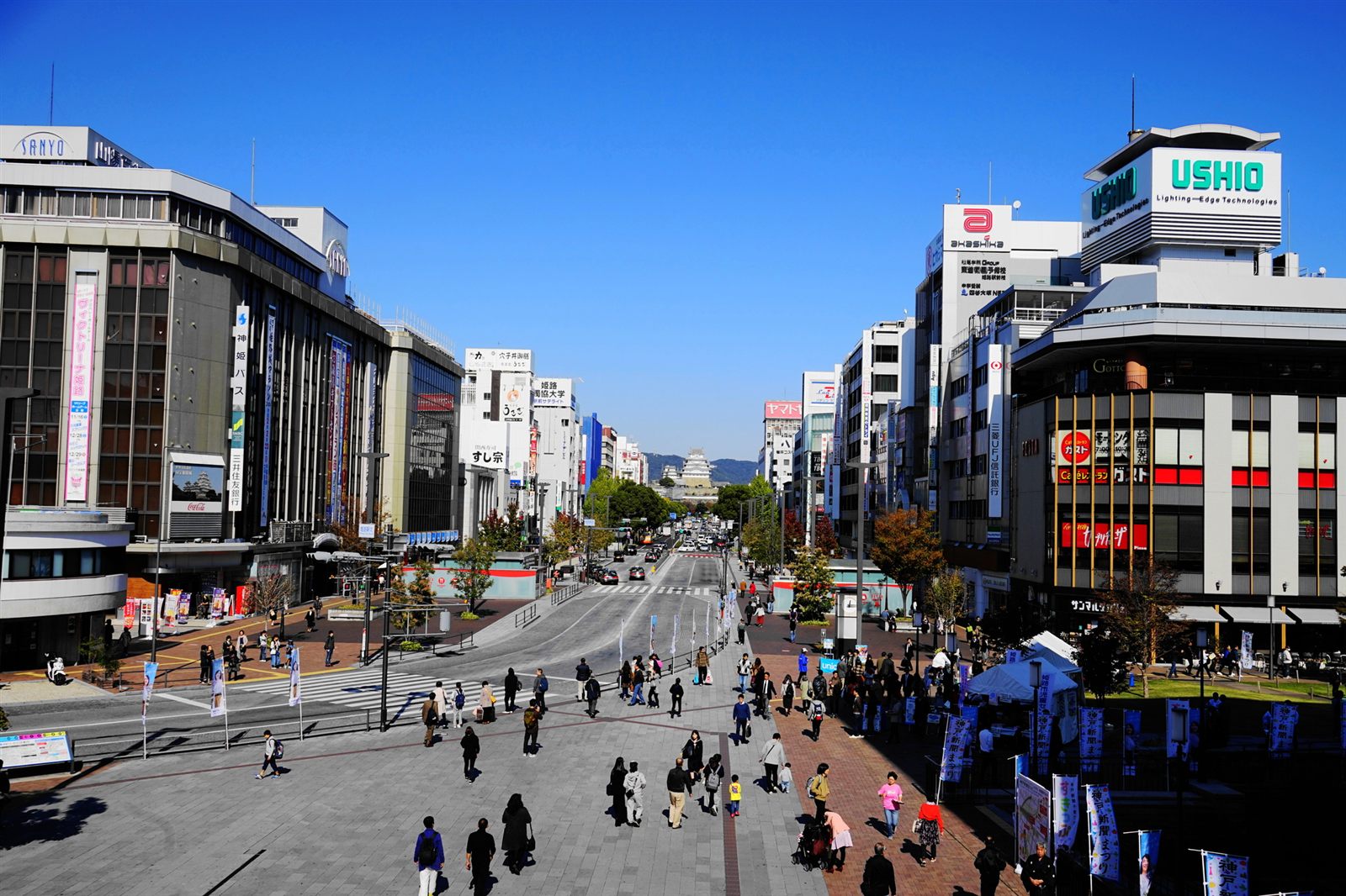 昼の姫路駅前。駅前広場の先、大手前通りの突き当たりに姫路城が見える。観光を終えた人たちが行き交う。