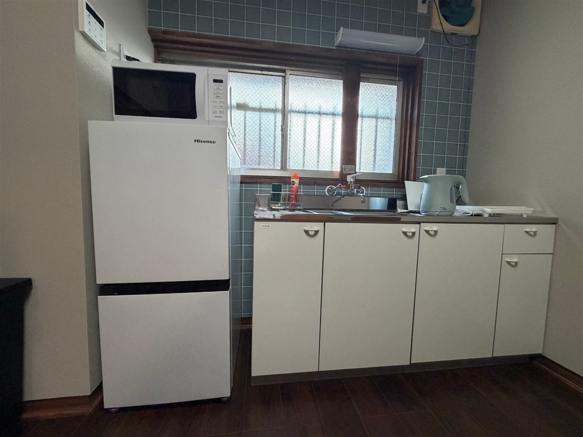 キッチンの一角。冷蔵庫の上に電子レンジ、シンクの横に電気ケトルが置かれている。